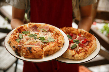 Waitress holds plates with fresh baked spicy sausage pizza. Restaurant service.