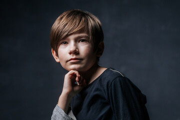 A close-up studio portrait of a young boy with a thoughtful expression, resting his chin on his...