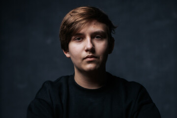 Fototapeta premium A close-up studio portrait of a young man in a black sweater, looking to the side with a calm and thoughtful expression. Soft lighting emphasizes his features against a dark background.