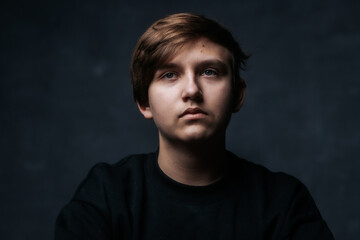 Fototapeta premium A close-up studio portrait of a young man in a black sweater, looking to the side with a calm and thoughtful expression. Soft lighting emphasizes his features against a dark background.