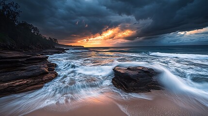Dramatic sunrise over ocean with rocky shoreline and waves.