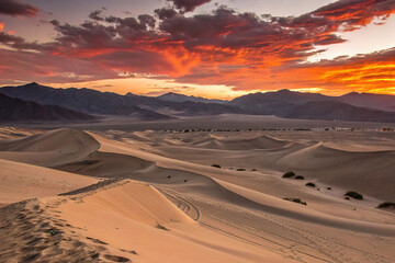 Vibrant sunset over desert dunes and mountains.