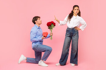 Guy standing on one knee with flowers and gift for Valentine's Day while offended lady rejecting...
