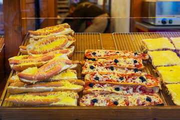 Hot dog buns with cheese and pizza slices on bakery display. Concept of casual street food and baked snacks