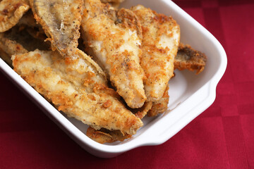 Fried fish background. Crispy fried cod fillet in breadcrumbs served on a white ceramic plate. Golden brown coating. Red tablecloth idea.