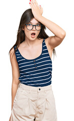 Young beautiful caucasian girl wearing casual clothes and glasses surprised with hand on head for...