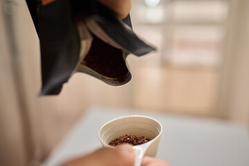 Pouring freshly ground coffee beans into a measuring cup for a perfect morning brew
