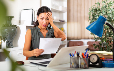 Portrait of upset asian female employee manager working with documents at working place