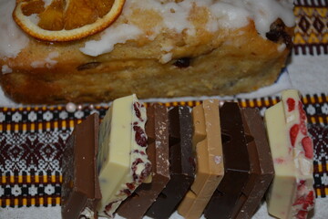 Bars of different white, dark and milk chocolate near cinnamon muffin on ornamented tablecloth
