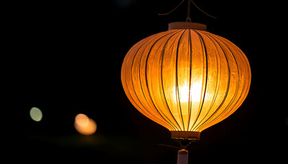 Fototapeta premium Warm, glowing orange paper lantern illuminates the night. Perfect for adding a touch of Asian-inspired ambiance to your design projects, websites, or travel brochures. Create a serene and peaceful