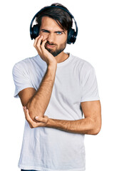 Hispanic man with blue eyes listening to music using headphones thinking looking tired and bored...