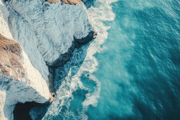 Ocean waves crash against the rocky cliffs under the bright sunlight along the coastline