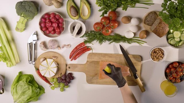 Skrapianie świeżego fileta z łososia sokiem z cytryny na drewnianej desce w otoczeniu warzyw, owoc&oacute;w i składnik&oacute;w &ndash; zdrowa kuchnia, przygotowanie dań z ryb