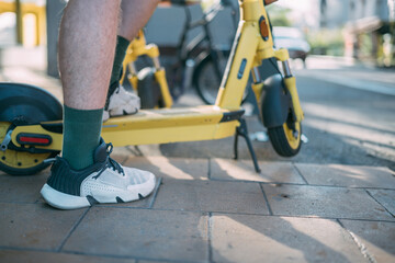 A man rents an electric scooter on the street. A young guy uses an application on his phone to rent a scooter in the city yard
