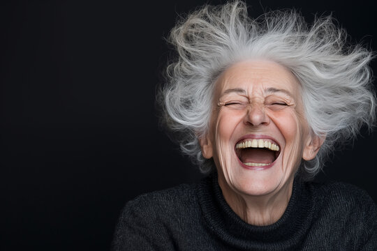 Senior citizen woman with crazy hair laughing with her eyes closed on a dark background with space for text