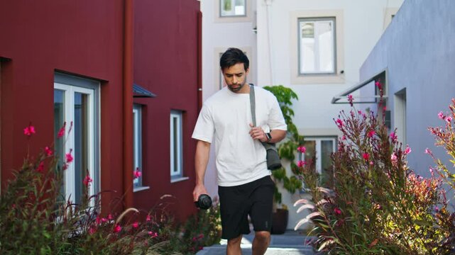 Sporty man walking outdoors with fitness gear surrounded by flowers and greenery