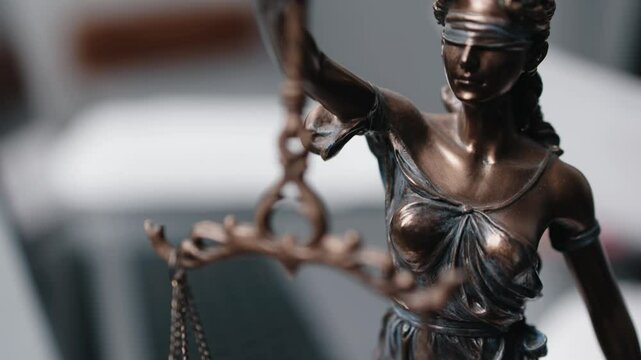 A lawyer works at their desk, sorting papers and entering data on a laptop. The statue of Themis stands nearby. Concept of legal decisions, work, and court proceedings.