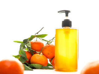 Soap dispenser filled with gold color liquid and fresh mandarins with green leaf. Organic skin care product made from natural ingredients. White background.