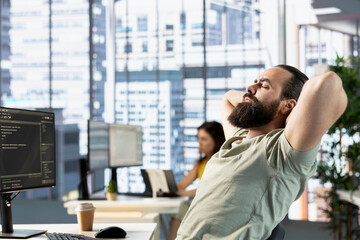 Fatigued admin fixing bad posture while managing cloud computing platforms to train machine learning models. Tired man stretching, trying to relax while monitoring and maintaining company systems