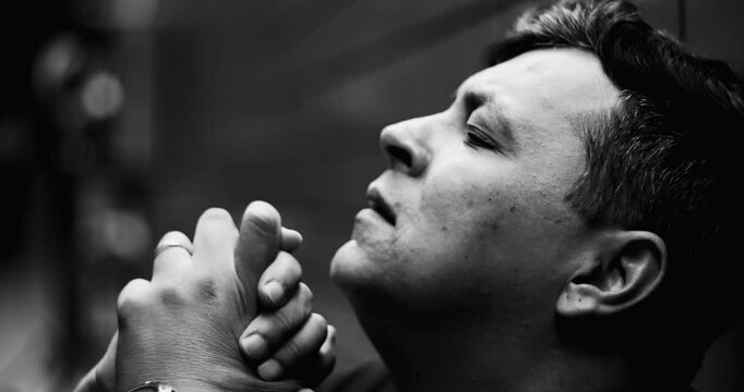 Close-up of distressed man with clasped hands, eyes closed, intense emotional pain, mental health crisis, depression, inner struggle, solitude, and despair in monochrome