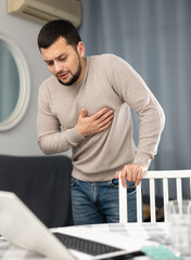 Young man touching his chest with hands while having heart pain and feeling unwell at home,...