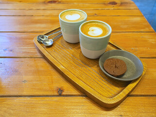 Two turmeric lattes with latte art and a chocolate cookie on wooden serving board