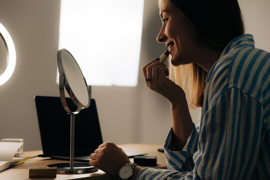 Smiling woman applying lipstick for a makeup tutorial
