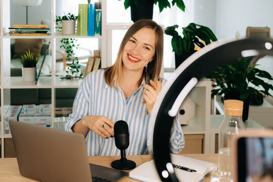 Smiling female YouTuber streaming with microphone in home studio 