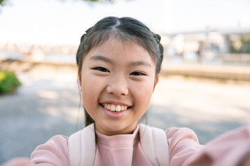 Smiling asian schoolgirl taking selfie outdoors in urban setting