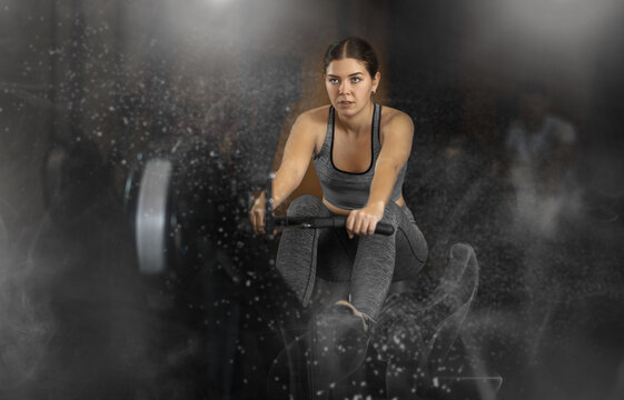 Woman performs exercises on a rowing machine, keeping the pace. Athletic woman in crossfit training doing intense exercises. Client in the gym monitors the figure and goes to training