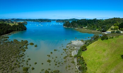 Obraz premium Aerial view of a beautiful bay with numerous sailboats. Coastal landscape with lush greenery and a clear blue sky. Tranquil scene. Mahurangi Harbour, Warkworth, Auckland, New Zealand