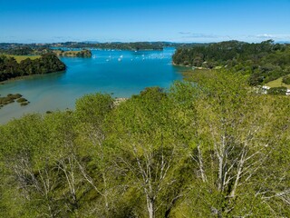 Aerial view of a picturesque bay with numerous sailboats. Lush green foliage surrounds the tranquil waterway. Sunny day. Mahurangi West, Warkworth, Auckland, New Zealand