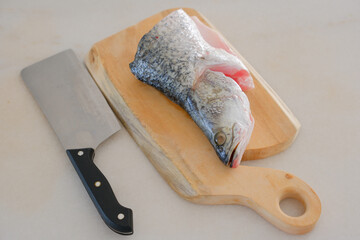 Fresh snapper fish on a wooden cutting board in a kitchen with a knife nearby