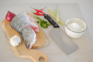 Fresh snapper fish on a wooden cutting board in a kitchen with a knife nearby