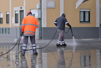 City street cleaning workers washing sidewalks with a water pressure gun