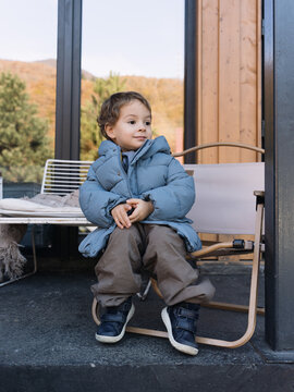 Stylish Todler Sitting On The Veranda Of A Street Cafe