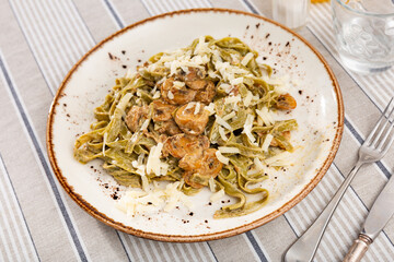 Hearty and simple homemade lunch. Italian past with mushrooms, dish is sprinkled with grated cheese. Cutlery and glass for drinks are prepared for meal.