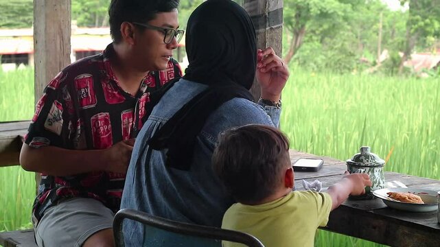 Asian muslim family doing chit chat talks while eating dinner, sitting on floor with low dining table, happy family