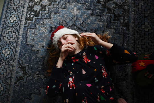 A child lies on the floor in Christmas pyjamas and a santa hat