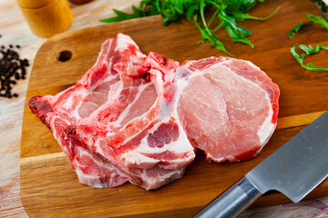 Slices of fresh uncooked pork loin steaks with black pepper and arugula.