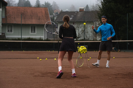 Man teaching girl how to play tennis on court.
 - Powered by Adobe