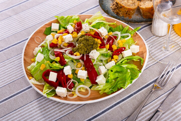 Appetizing salad of fresh vegetables served with feta cheese and pesto on plate
