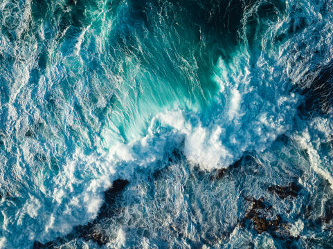 Top down aerial view of ocean wave crashing on coastline at sunset 