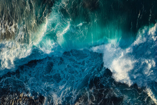 Top down aerial view of ocean wave crashing on coastline at sunset 