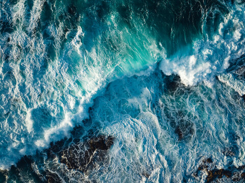 Top down aerial view of ocean wave crashing on coastline at sunset 
