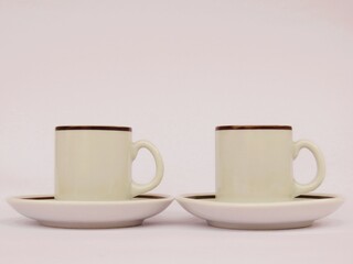 Two white ceramic cups and saucers with brown rim on a white background.