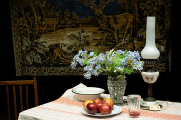 Still life with kerosene lamp, lilies of the valley and apples against the background of a carpet with deer