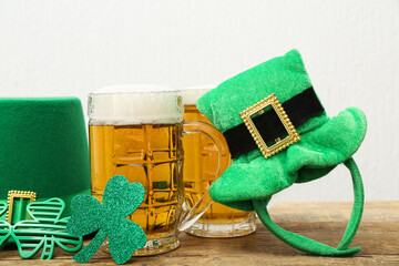 Mugs of beer with leprechaun hats, plastic eyeglasses and paper clover on wooden table against...