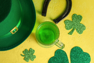 Mug of green beer with leprechaun hat, horseshoe and paper clovers on yellow grunge background. St....
