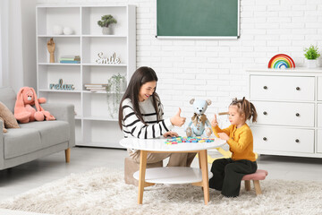 Cute little girl and teacher with letters showing thumbs-up at home